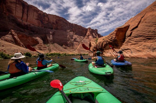 People kayak down a river with canyon walls in the background.