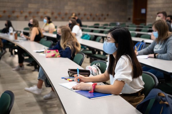 Students are pictured in class, taking notes and wearing masks