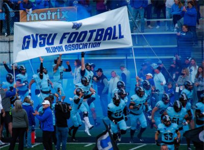Grand Valley football players run underneath a banner showing support.