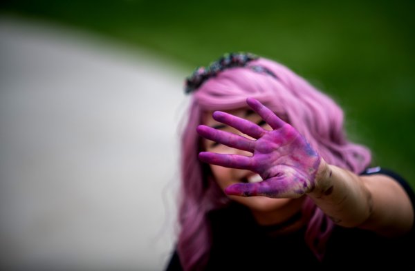 A person reaches their hand out in front of their face showing purple chalk dust covering the surface of their hand