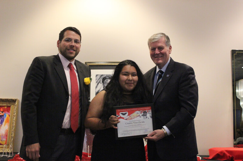three people standing, woman in center holds certificate