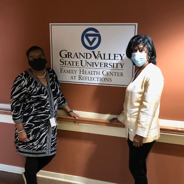 Reflections staff members Crystal Cunningham, left, and Roslyn Shackelford stand in the clinic by sign that reads GVSU Family Health Center.