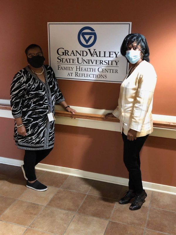 Reflections staff members Crystal Cunningham, left, and Roslyn Shackelford stand in the clinic by sign that reads GVSU Family Health Center.