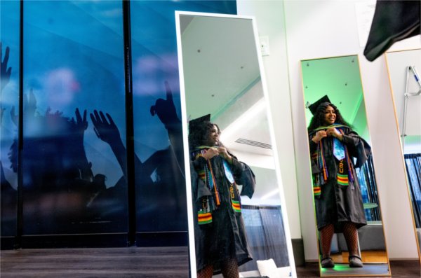  A college graduate is reflected in two mirrors as she adjusts her academic regalia. 