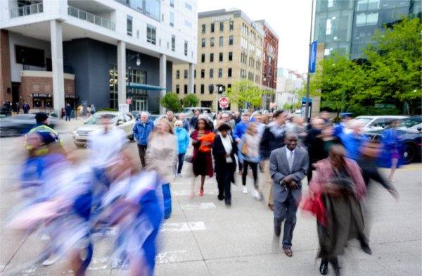  With a slow motion blur, students and their families cross the street in a downtown city scape.