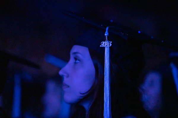 Close up photo of a person bathed in dark blue/purple light, the 2023 on their tassel stands out.