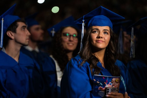 A person has a pensive look as they sit holding their Commencement program. 