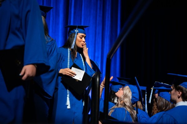 A person dressed in a cap and gown has their hand on their mouth in a gesture to symbolize blowing a kiss to her friend below. 