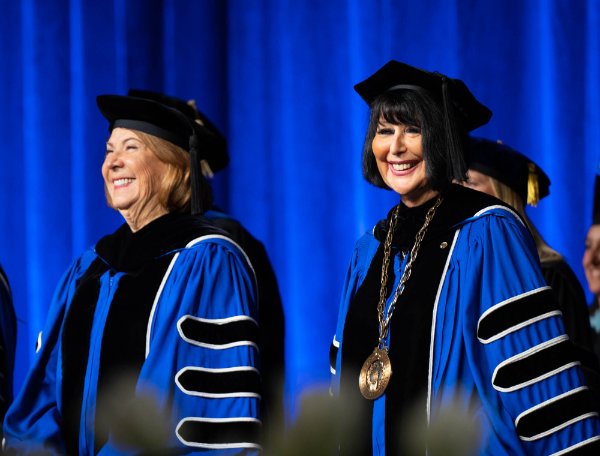 Two people wearing academic regalia stand on stage during a Commencement ceremony. 