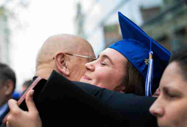  A person wearing a graduation hat hugs a person.