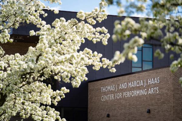 The building name on the outside of the Thomas J. and Marcia J. Haas Center for Performing Arts is framed by white flowers.