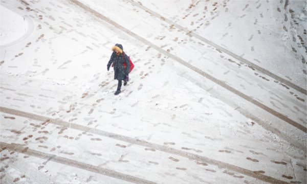  A person wearing a winter coat walks over a snow-covered sidewalk. 