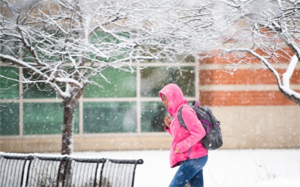  A college student pulls a pink hood over their head to keep themselves out of the snowy conditions. 