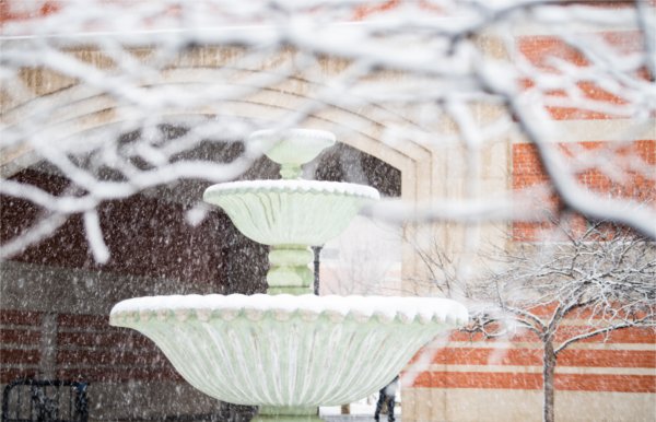  A fountain is seen in a snowy scene on a college campus. 