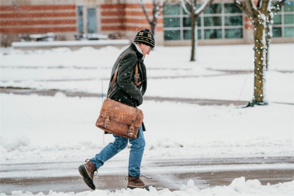 A person carrying a leather bag walks through campus on a snowy day.  