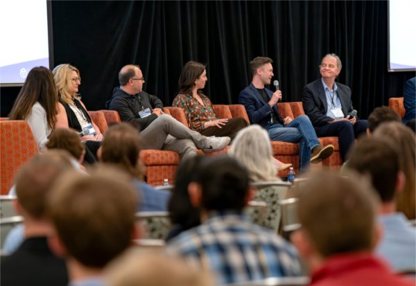 Panelisrs on a dais answer a question from an audience member.