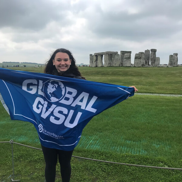 Ashley Brown holds a GVSU study abroad flag in front of Stonehenge.