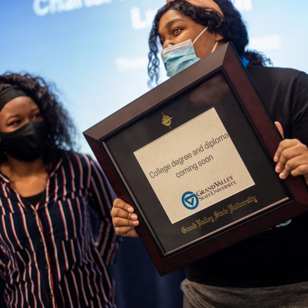 A smiling student holds a diploma frame during a luncheon presented by the Charter Schools Office.