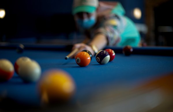 A student aims a pool cue at colorful billiard balls on a pool table. 