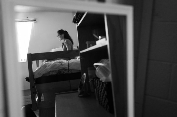 A person is reflected in a mirror sitting on her bed studying. 