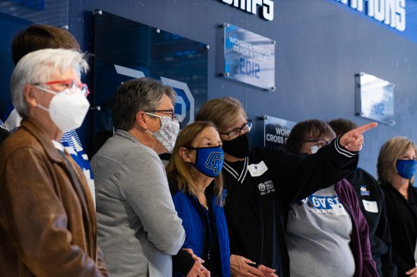 attendees all in masks stand with Joan Boand at wall