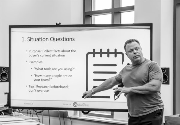 A man stands in front of a large presentation screen, gesturing as he teaches a lesson on &#8220;Situation Questions.&#8221;
