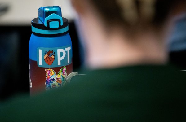 A water bottle has the word the letter "I," an image of an anatomical heart, then the letters "PT." A person's back in the foreground.