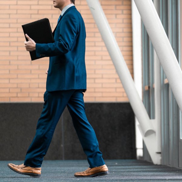 A person in a navy blue suit walking and carrying a folder.