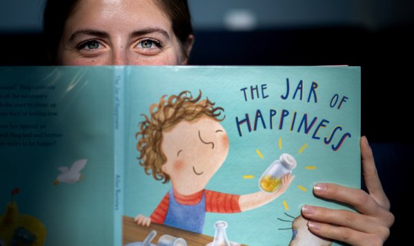 A college student peeks over the cover of the book, "The Jar of Happiness."  