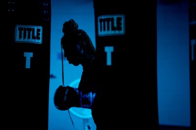 A high school student is silhouetted against a blue wall as they practice boxing. 