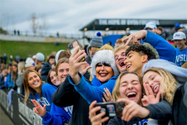  A group of people on the sidelines smile while taking a selfie. 