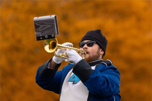  A band member in a blue and white uniform plays the trumpet with a blurred orange background.