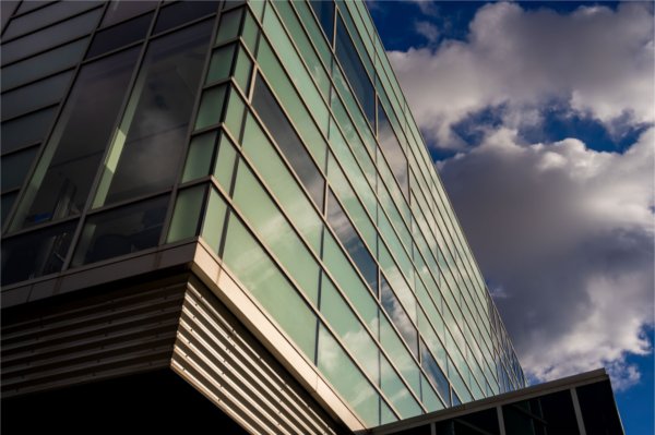  A modern glass building with reflective surfaces and a cloudy sky in the background.