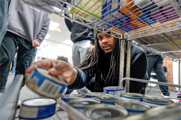  A person crouching and reaching for a can on a metal shelf in a stocked pantry.