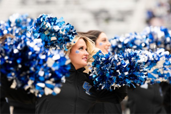  Dancers with blue and silver pom-poms in action, wearing black jackets with &#8220;GV&#8221; logos.