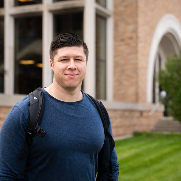 Mathias Mapes-Pearson poses in front of a building. He is wearing a backpack.