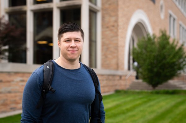 Mathias Mapes-Pearson poses in front of a building. He is wearing a backpack.