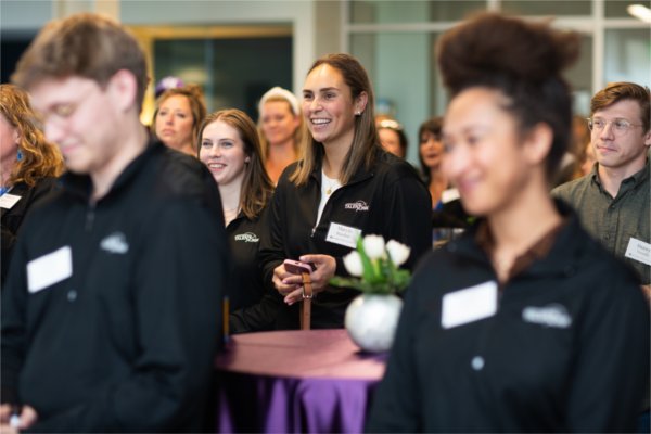 Several people in an audience smile while watching someone speak.