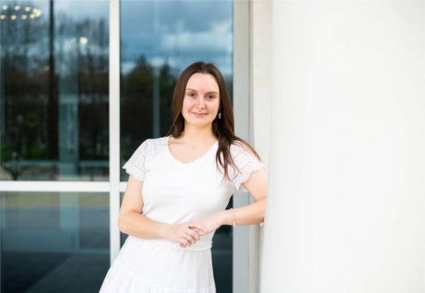 A person smiles while leaning an elbow against a wall