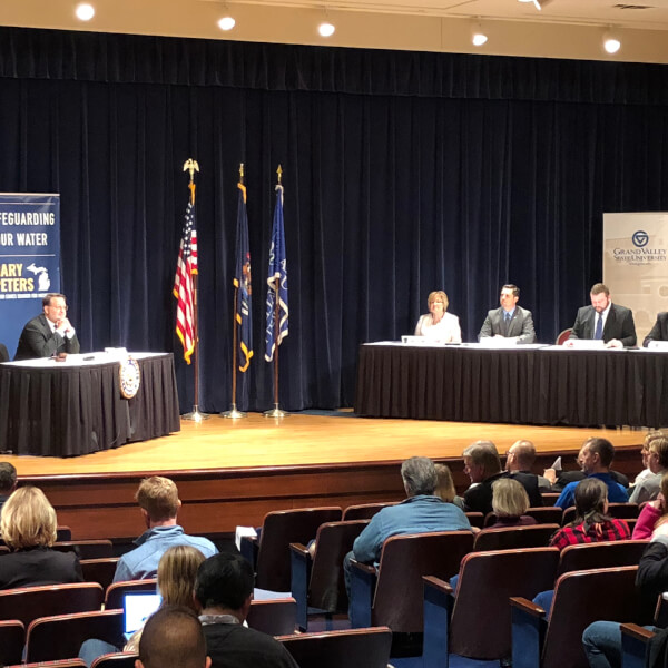 Four panelists sit at a table on the right side of the stage at Loosemore Auditorium on Grand Valley's Pew Grand Rapids Campus. Senator Gary Peters, a democrat from Michigan, sits at a table on the left side of the stage.