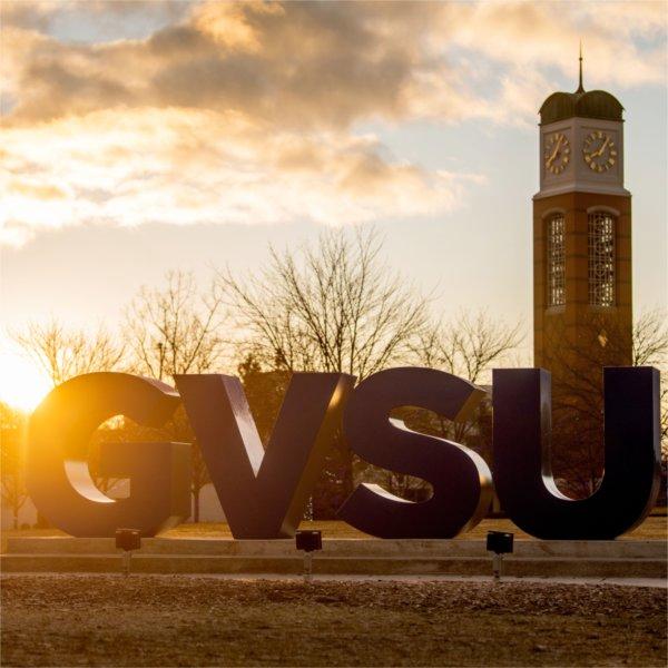 The carillon is seen at a sunrise behind the GVSU letters.