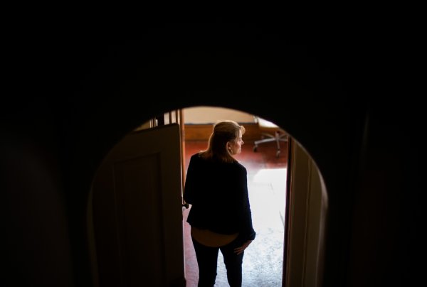  A person stands in an arched doorway with their back to the camera and face turned to the right, partly silhouetted but can see their face. 