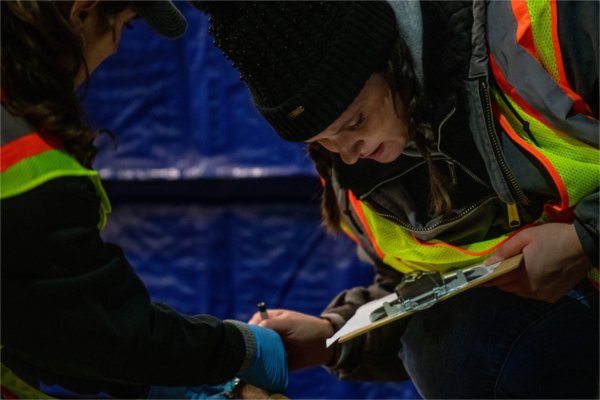 Pople wearing yellow vests, one holding a clipboard, study the leg of a deer.