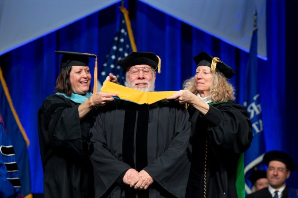 Apple co-founder Steve Wozniak is hooded by Provost Jennifer Drake, right, and his wife, Janet Hill, while receiving an honorary degree during Commencement at Van Andel Arena on May 1.
