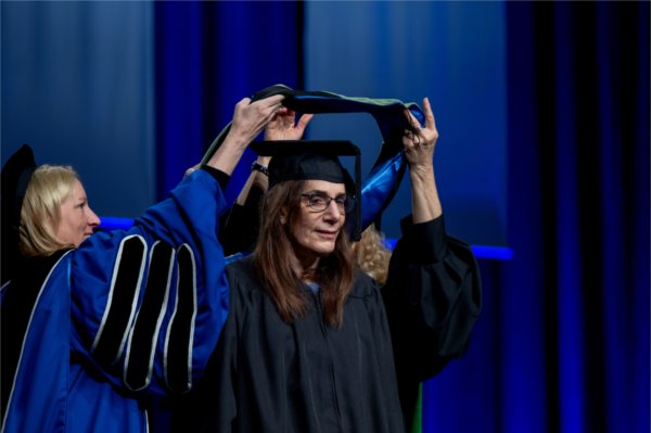Founder of Epic Systems Judith R. Faulkner is hooded by Provost Jennifer Drake and Tina Freese Decker, CEO of Corewell Health,  left, while receiving an honorary degree during Commencement at Van Andel Arena on May 2.