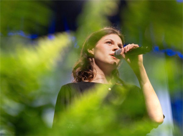 A person singing with green foliage in the foreground.
