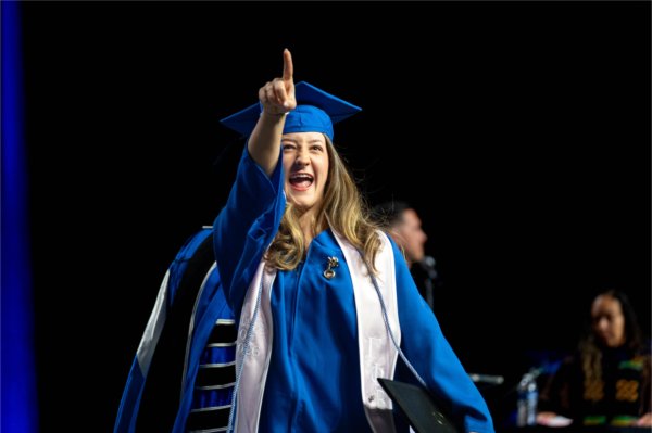 A graduate in a blue cap and gown pointing
