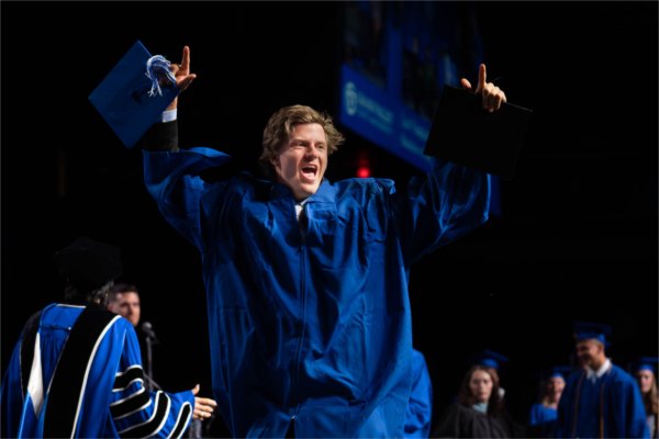 A graduate in a blue cap and gown pointing