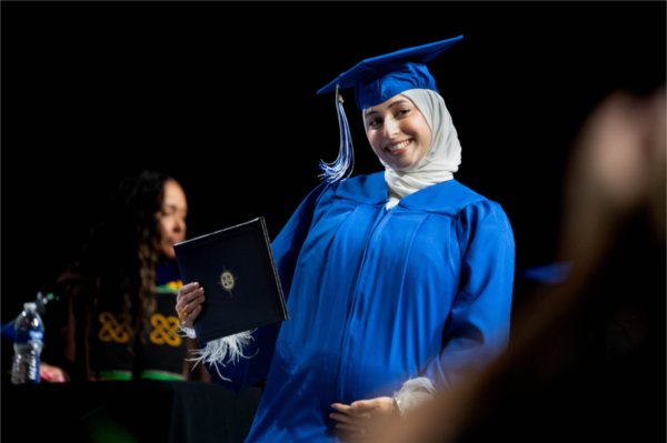 A graduate in a blue cap and gown holding a diploma