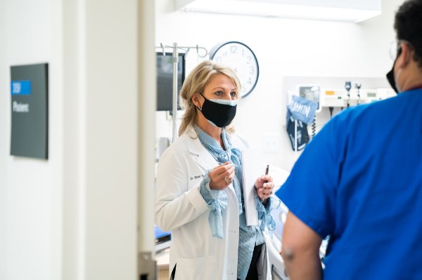 nursing faculty member in white coat talks to a student in blue scrub shirt